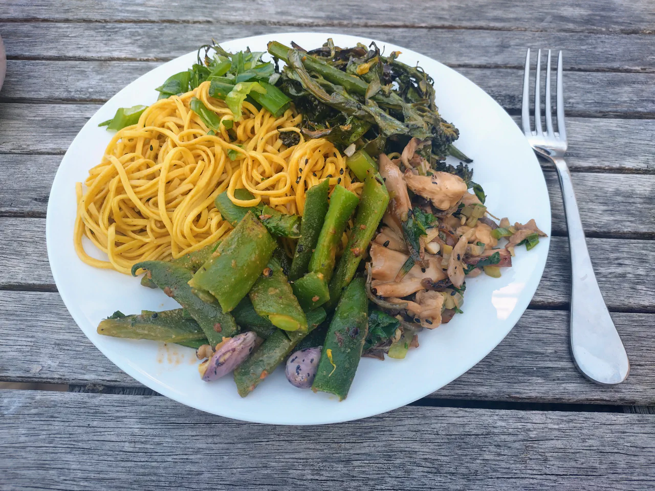 Plated noodle stir-fry with pink oyster mushrooms, green beans, purple sprouting broccoli and fresh herbs on a white plate